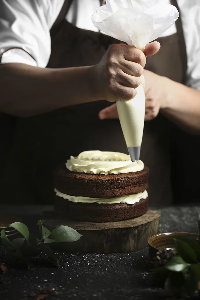 Mãos com saco de confeitar recheando um bolo de chocolate.